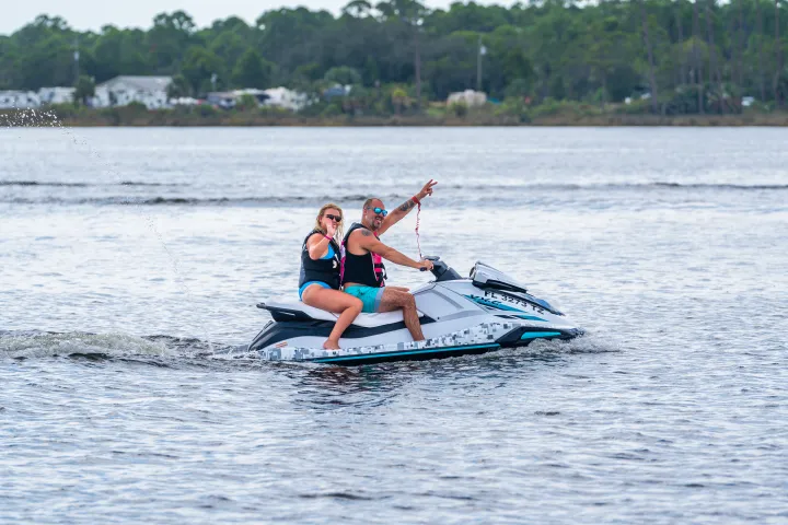 Two people riding a jet ski on a lake, wearing life jackets.