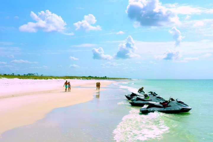 Beach scene with people walking and jet skis on shore under a cloudy sky.