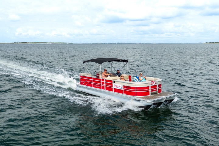 Red pontoon boat with canopy on open water under a cloudy sky.