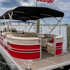 Red pontoon boat docked at marina under cloudy sky.