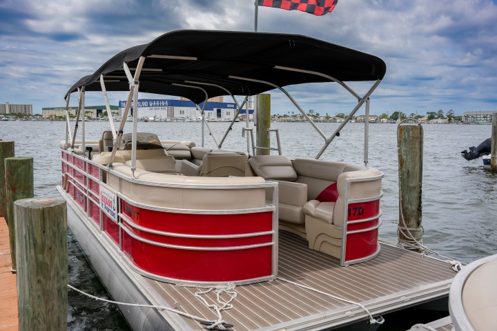 Red pontoon boat docked at marina under cloudy sky.