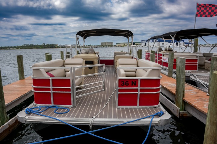 Red pontoon boat docked at a marina under a cloudy sky.