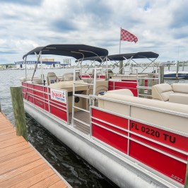 Red pontoon boat docked on a wooden pier with a checkered flag.