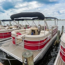 Red and white pontoon boats docked at a pier under a cloudy sky.