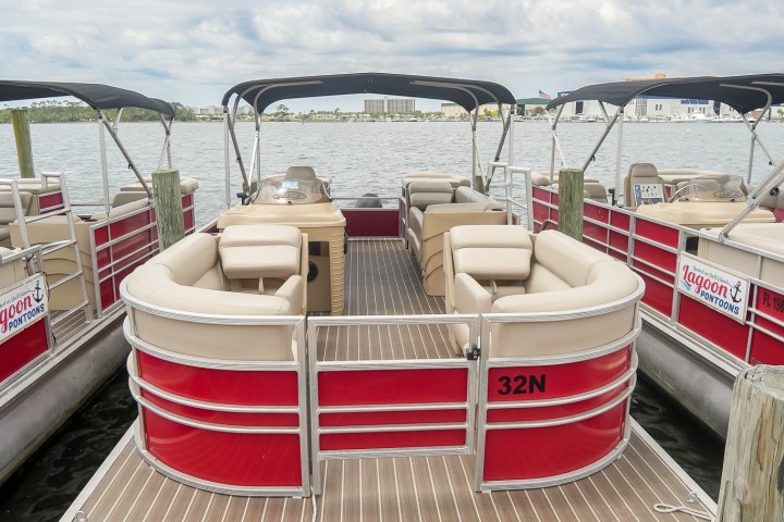 Red and white pontoon boat docked at a harbor under cloudy sky.