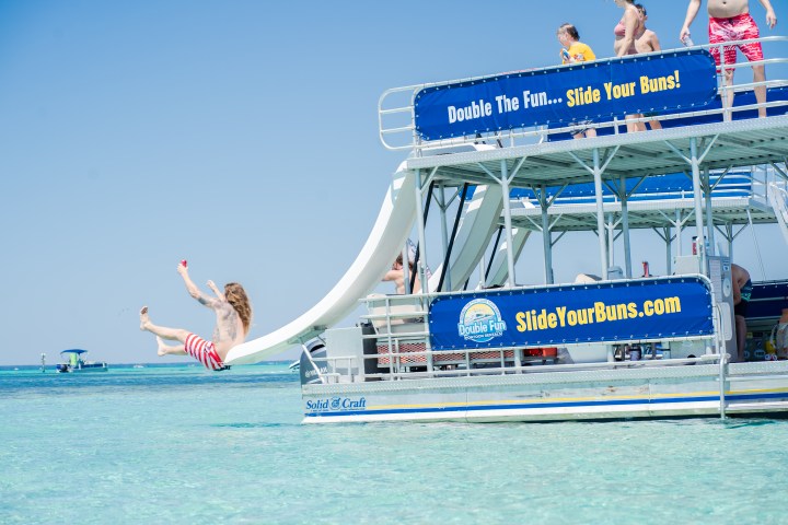 Person sliding off boat slide into clear blue water.