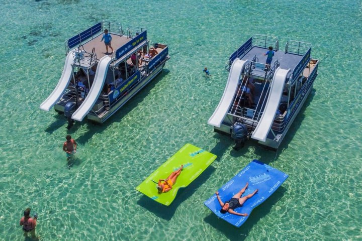 People on rafts and boats in clear water with slides.