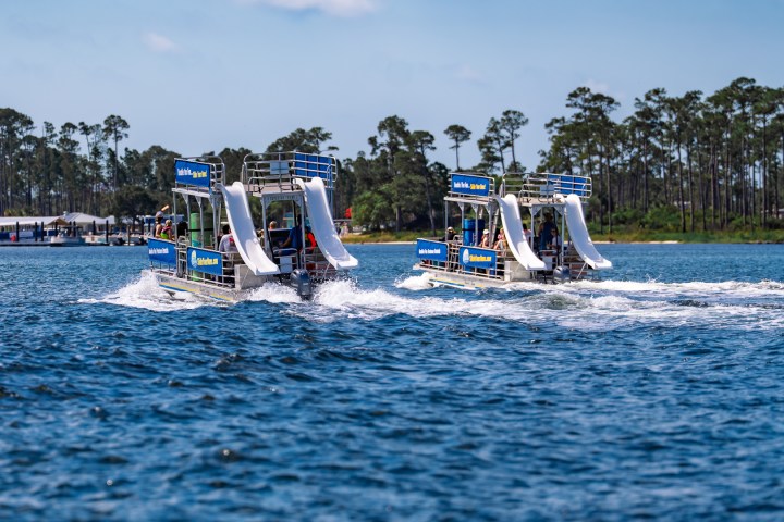 Two boats with slides on a lake, trees in the background, sunny day.