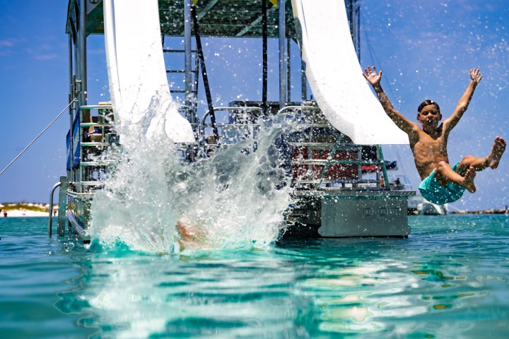 Two kids splash into the water from a slide on a boat.