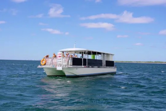 A white boat with people on a blue ocean under a partly cloudy sky.