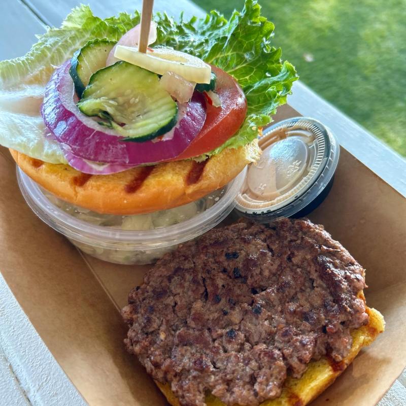 Deconstructed burger with bun, patty, vegetables, and sauce in a cardboard tray.