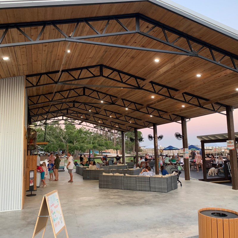 Open pavilion with people seated and walking, surrounded by trees at sunset.