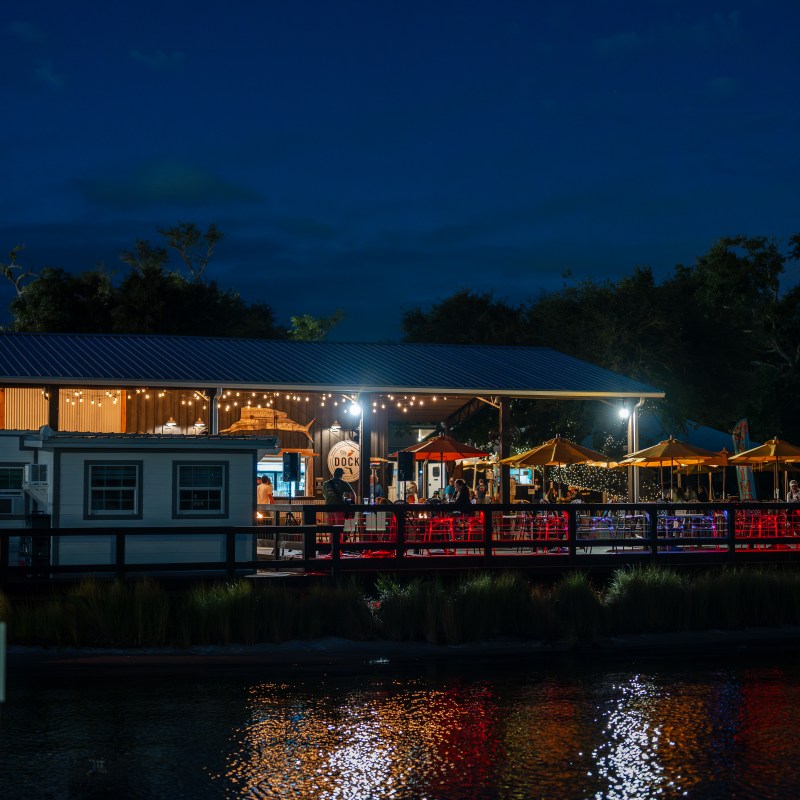 Outdoor restaurant by the water at night, illuminated with lights.