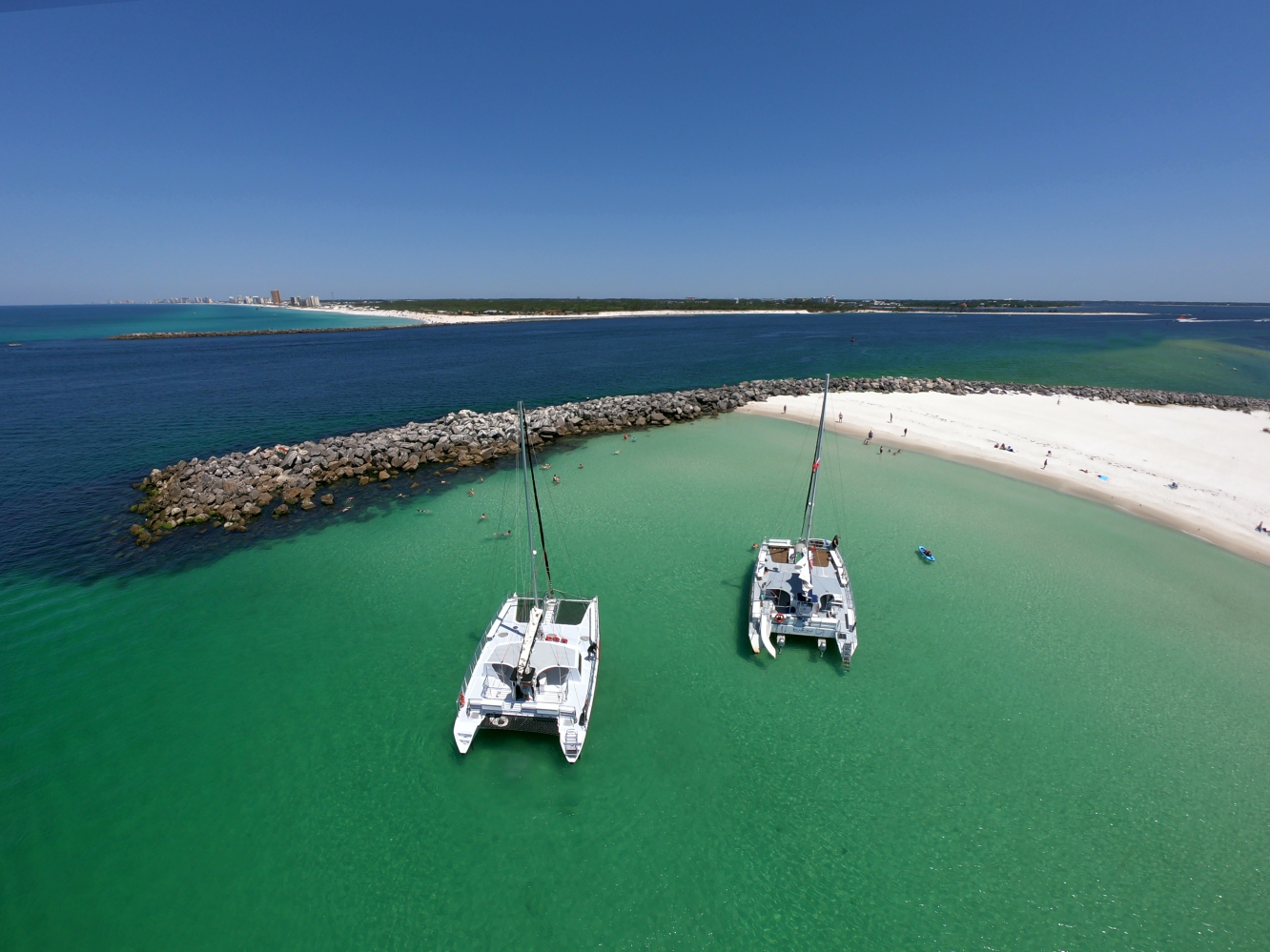 Two catamarans by a sandy beach with turquoise water and a clear blue sky.