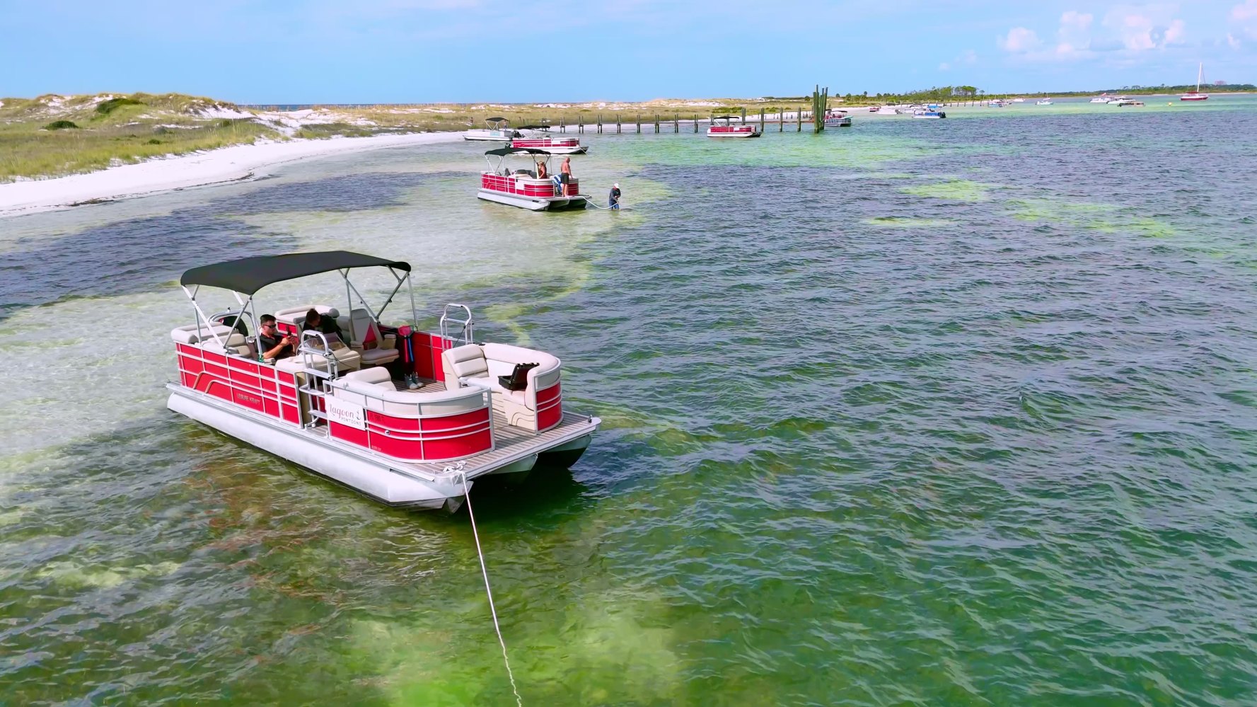 Red pontoon boats in shallow, clear water near sandy shore.